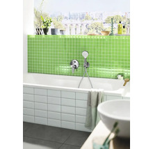 Modernes Badezimmer mit weißer Badewanne, Armatur, grünen Mosaikfliesen und einer Fensterfront mit Stadtblick.