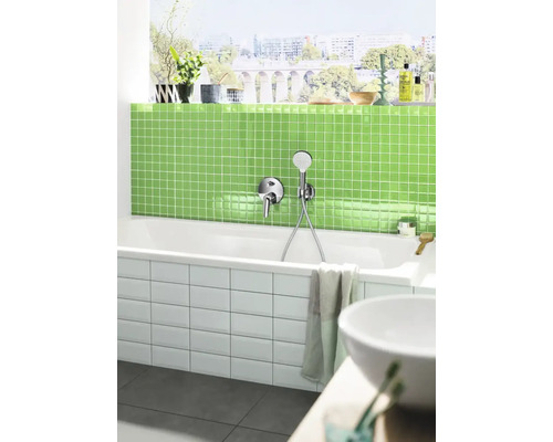 Modernes Badezimmer mit weißer Badewanne, Armatur, grünen Mosaikfliesen und einer Fensterfront mit Stadtblick.