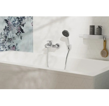 Moderne Badewannenarmatur mit Handbrause an einer weiß gefliesten Wand über einer Badewanne mit floralem Wandbild.
