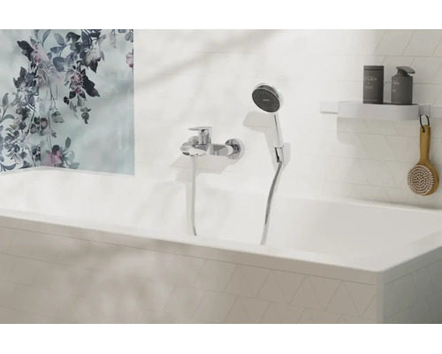 Moderne Badewannenarmatur mit Handbrause an einer weiß gefliesten Wand über einer Badewanne mit floralem Wandbild.