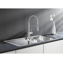 Moderne Edelstahl Küchenspüle mit Abtropffläche und professioneller Küchenarmatur mit Schlauchbrause auf einer dunklen Arbeitsplatte.