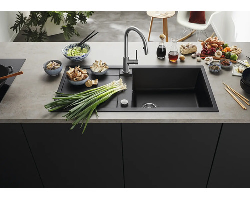 Moderne schwarze Einbauspüle mit Abtropffläche und Edelstahlarmatur in einer organisierten Küche mit frischen Zutaten auf der Arbeitsplatte.