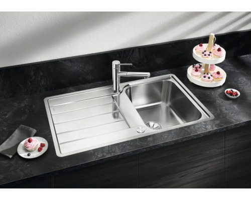 Edelstahl Einbauspüle mit Abtropffläche und moderner Küchenarmatur eingebaut in einer dunklen Arbeitsplatte mit Küchenaccessoires.