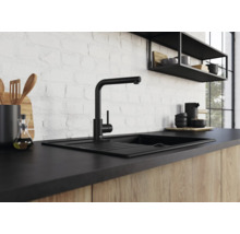 Moderne schwarze Küchenarmatur mit Spülbecken vor einer weißen Ziegelwand in einer Küche mit Holzfronten.