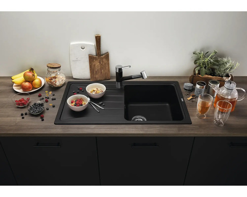 Moderne schwarze Einbauspüle mit Abtropffläche und passender Armatur in einer Küche mit Arbeitsplatte in Holzoptik und dunklen Küchenfronten.