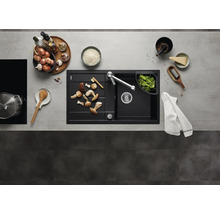 Moderne schwarze Einbauspüle mit Abtropffläche und Küchenarmatur in einer organisierten Küche mit Kochutensilien und frischen Lebensmitteln.