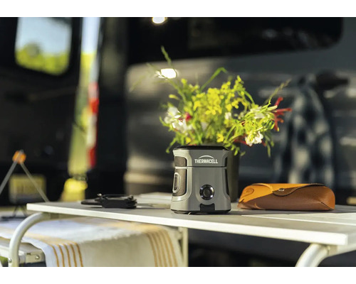Thermacell Mückenschutzgerät auf einem Camping-Tisch vor einem Wohnmobil im Freien.