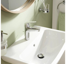 Moderne Waschtischarmatur in Chrom auf einem weißen Waschbecken in einem Badezimmer mit Spiegel und Accessoires.