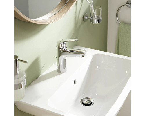 Moderne Waschtischarmatur in Chrom auf einem weißen Waschbecken in einem Badezimmer mit Spiegel und Accessoires.