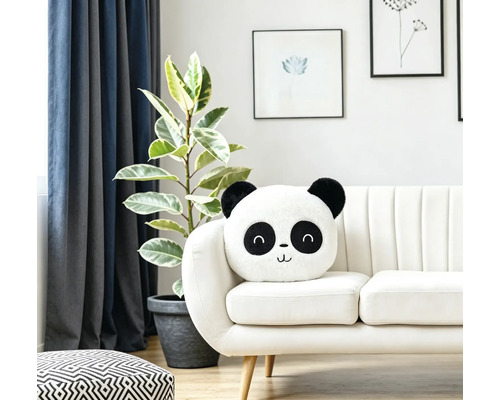 Ein flauschiges Panda Kissen auf einem modernen hellen Sofa in einem Wohnzimmer mit Zimmerpflanze und Wandbildern.