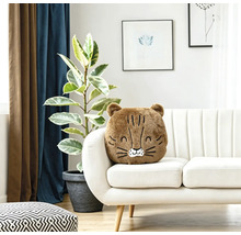 Ein weiches, flauschiges Dekokissen in Tierform liegt auf einem hellen Sofa in einem modern eingerichteten Wohnzimmer mit Zimmerpflanze.
