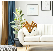 Ein weiches Dekokissen in Form eines Rehkopfes auf einem hellen Sofa in einem modern eingerichteten Wohnzimmer.