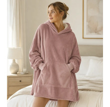 Eine Frau trägt einen übergroßen Kapuzenpullover aus weichem Plüschmaterial mit Kängurutasche in einem hellen Schlafzimmer.