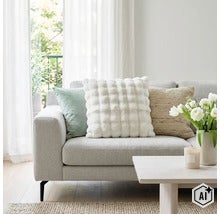 Ein helles Wohnzimmer mit einem Sofa, das mit drei verschiedenen Zierkissen dekoriert ist, sowie einem Couchtisch mit einer Vase voller Blumen. (Image AI modified or generated)