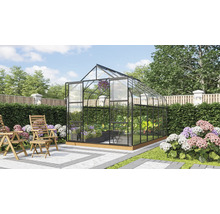 Freistehendes Gewächshaus mit Glaswänden und Metallrahmen in einem gepflegten Garten mit Holzstühlen auf einer Terrasse.