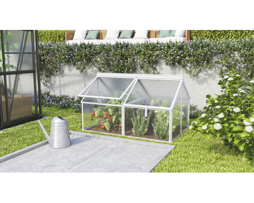 Ein kleines Frühbeet aus Aluminium und Hohlkammerplatten im Garten neben einer Gießkanne mit zwei aufklappbaren Dachfenstern für den Anbau.