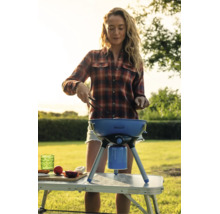 Eine Frau grillt mit einem mobilen Gaskugelgrill auf einem Campingtisch im Garten.