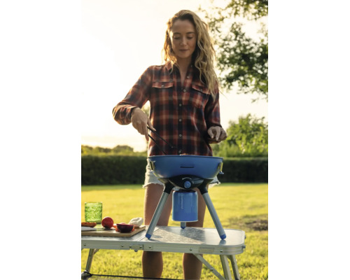 Eine Frau grillt mit einem mobilen Gaskugelgrill auf einem Campingtisch im Garten.
