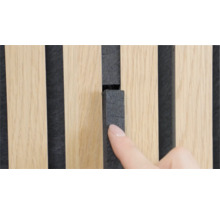 Hand berührt ein Akustikpaneel mit Holzlamellen und Filzrückwand zur Schallabsorption.