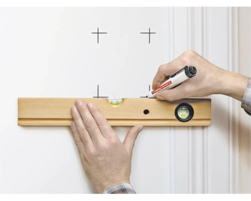 Eine Hand hält eine Wasserwaage aus Holz an einer Wand, während die andere Hand mit einem Edding Marker Markierungen setzt.