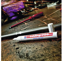 Edding 750 Lackmarker auf einem Holztisch mit einem Metallstab und Funkenflug im Hintergrund