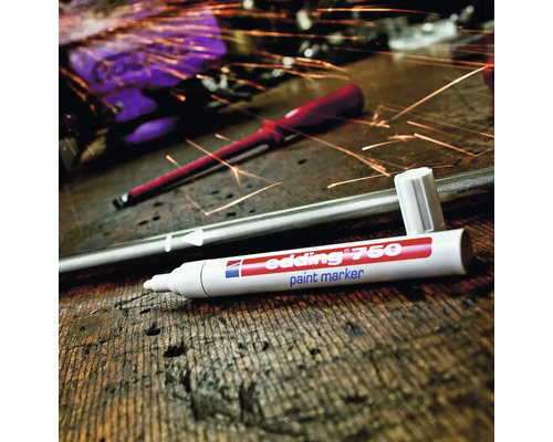 Edding 750 Lackmarker auf einem Holztisch mit einem Metallstab und Funkenflug im Hintergrund