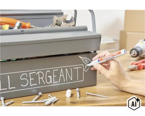 Eine Hand beschriftet mit einem Edding 750 Lackmarker einen grauen Werkzeugkasten aus Metall auf einem Holztisch. (Image AI modified or generated)