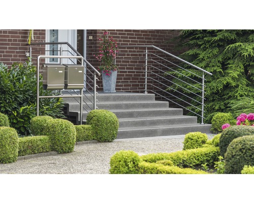 Außenaufnahme eines Hauseingangs mit Treppe, Edelstahlgeländer und zwei Briefkästen vor einem gepflegten Garten.