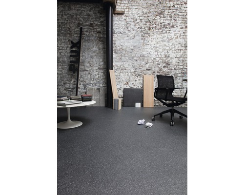 Innenraum mit dunklem Bodenbelag, Bürostuhl und weißem Tisch vor einer Ziegelwand
