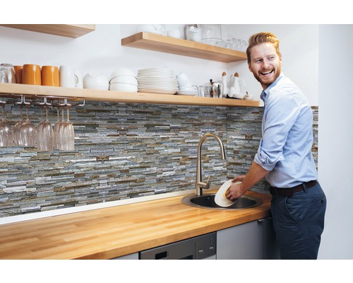 Wandbelag PVC Ceramics Stone wall grau 67,5 x 400 cm Küchenszene mit Steinwandpaneelen, Spüle und Mann beim Abwaschen