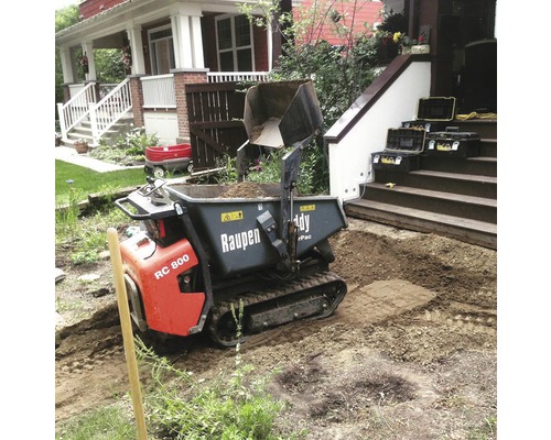 Motorbetriebene Schubkarre beim Abladen von Erde in einem Garten.