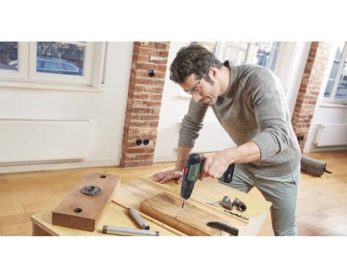 Ein Mann bohrt mit einer Bohrmaschine ein Loch in ein Holzbrett.