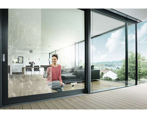 Frau putzt Fenster in einem modernen Wohnzimmer mit Glasschiebetüren und Terrasse.