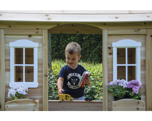 Junge spielt in einem Holzspielhaus mit Spielzeugfahrzeugen