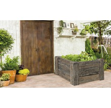 Garten mit Hochbeet aus Holz, Pflanzen und Gartengeräten vor einer Holzwand