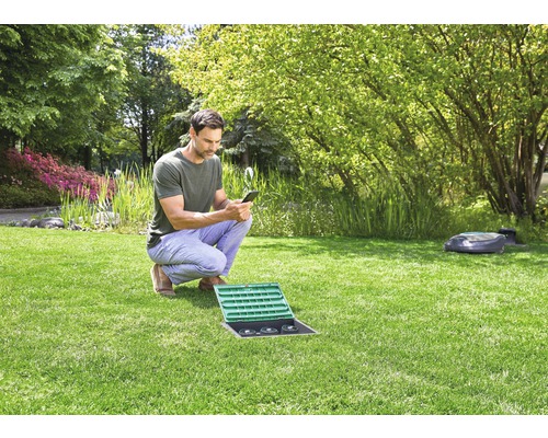Mann bedient Bewässerungssteuerung mit Smartphone im Garten