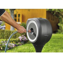 Gartenszene mit Schlauchbox und Person, die einen Gartenschlauch anschließt.