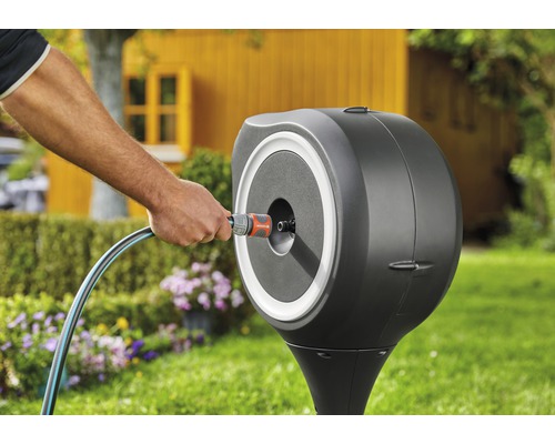 Gartenszene mit Schlauchbox und Person, die einen Gartenschlauch anschließt.