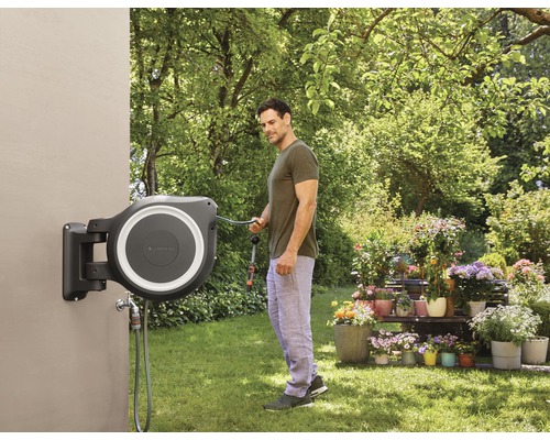 Garten Szene mit einem Mann, der einen Gartenschlauch benutzt, der an einer automatischen Schlauchbox befestigt ist