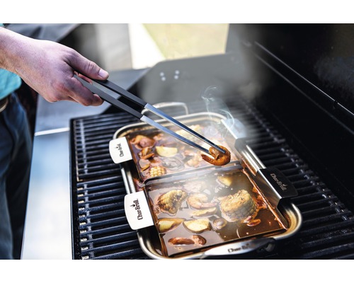 Grillschale mit Meeresfrüchten und Gemüse wird mit einer Grillzange angehoben