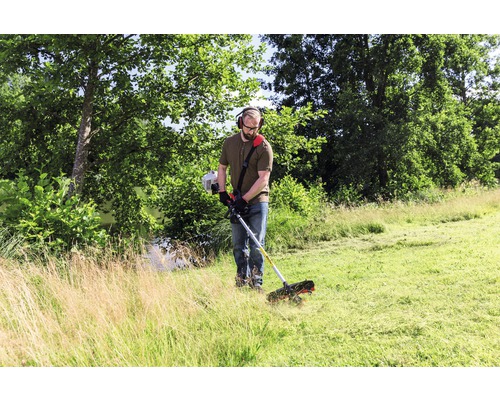 Ein Mann mit Kopfhörern benutzt einen Rasentrimmer im Garten.