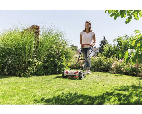 Frau benutzt Spindelmäher im Garten.