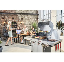 Szene im Freien mit einem Grill, einer Person, die Essen serviert, und einer Gruppe von Leuten, die an einem Tisch sitzen