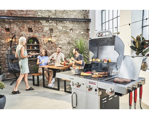 Szene im Freien mit einem Grill, einer Person, die Essen serviert, und einer Gruppe von Leuten, die an einem Tisch sitzen