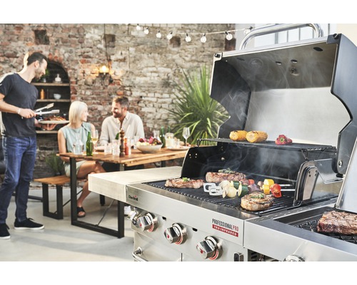 Szene mit Grill, auf dem Speisen zubereitet werden, und Personen, die an einem Tisch sitzen
