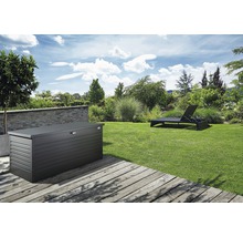 Gartenszene mit einer Gerätebox aus Metall auf einer Holzterrasse und einer Sonnenliege auf dem Rasen