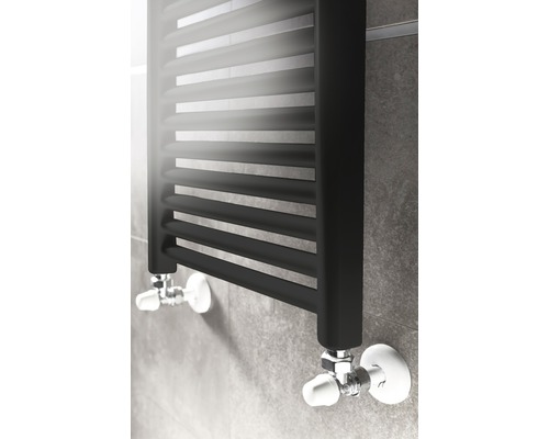 Schwarzer Handtuchheizkörper mit Ventilen an einer grauen Wand