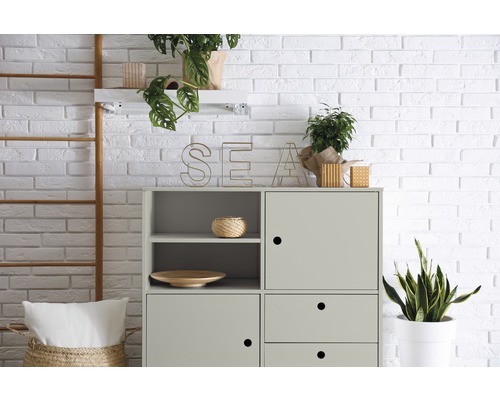 Helles Zimmer mit einer Kommode, Dekoration und Pflanzen vor einer Backsteinwand.