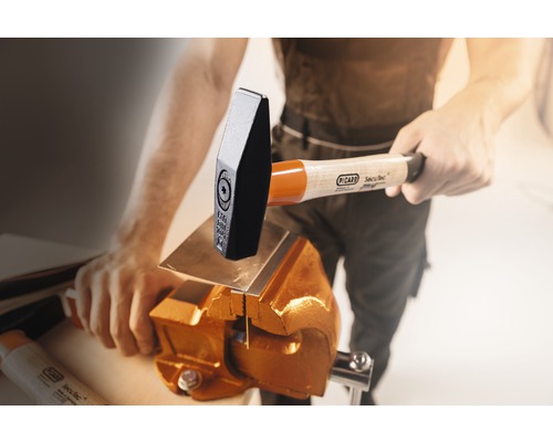 Ein Mann verwendet einen Hammer, um ein Metallstück in einem Schraubstock zu bearbeiten.