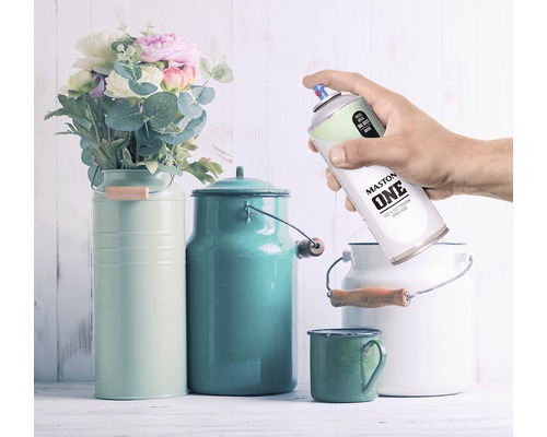 Dekorative Szene mit Blumen, farbigen Milchkannen und eine Hand, die eine Dose Maston One Sprühfarbe hält.